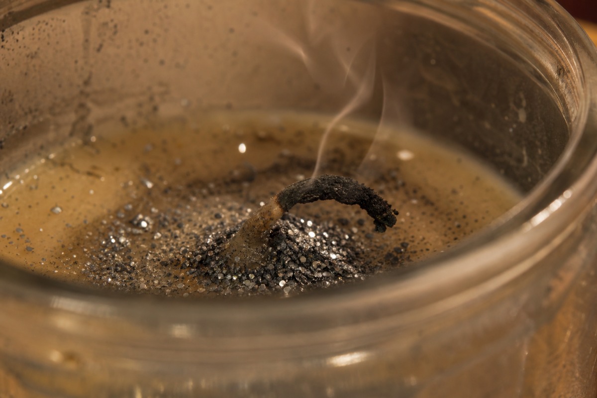 A bent, charred wick coated in accumulated silver glitter in solidified wax, the candle extinguished.
