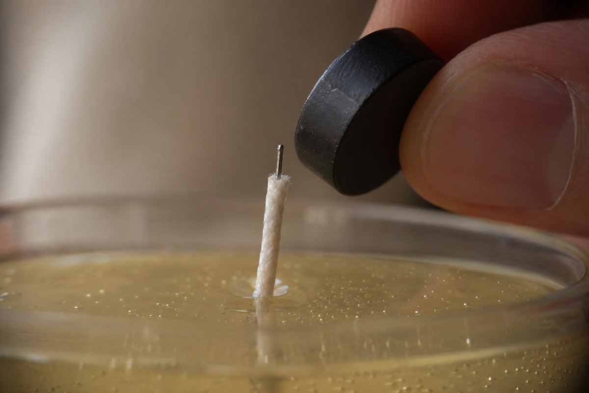 Close-up of a pulled-out wick with a thin metal core and a small magnet held next to the wick's metal centre