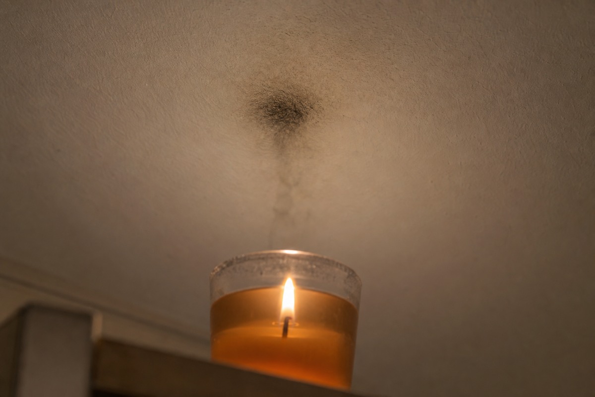 A dark soot mark on a white ceiling directly above a burning gel candle in a glass tumbler