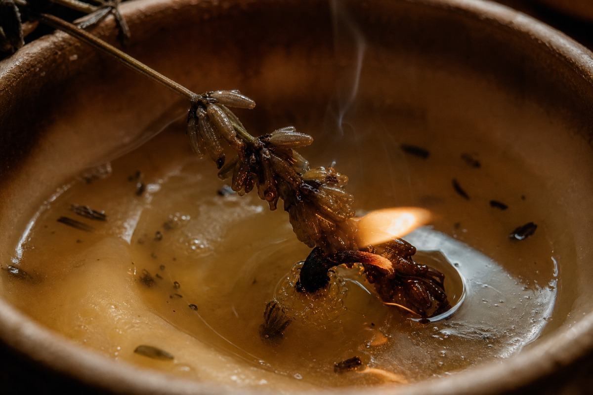 A dried lavender spike soaked with wax leaning onto the wick in an uneven pool of melted wax